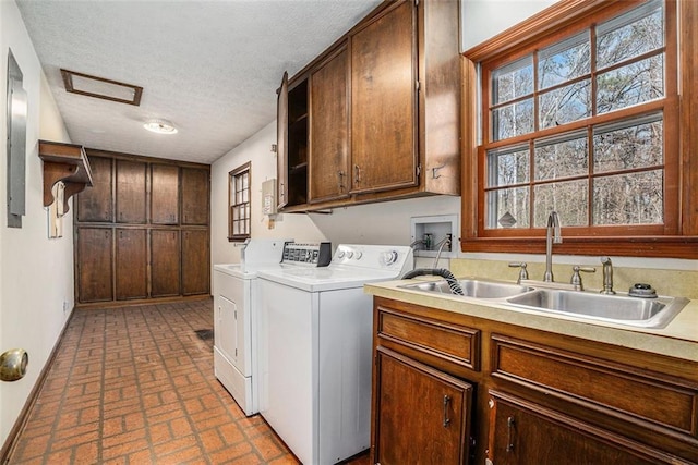 laundry area featuring brick floor, washing machine and clothes dryer, cabinet space, a sink, and a textured ceiling