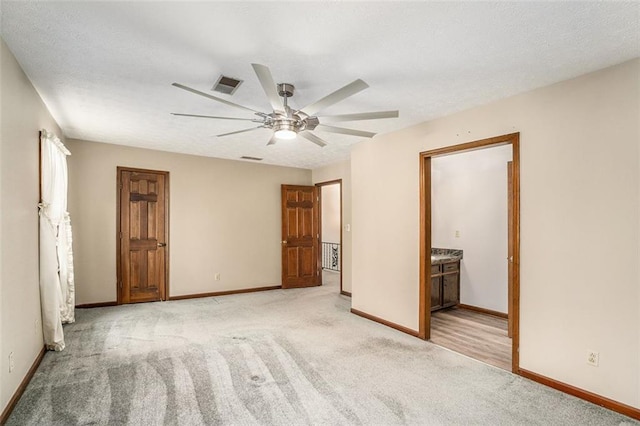 unfurnished bedroom featuring visible vents, a ceiling fan, light carpet, ensuite bath, and baseboards