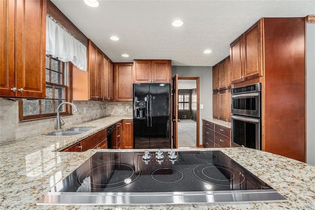 kitchen featuring decorative backsplash, light stone counters, black appliances, a sink, and recessed lighting