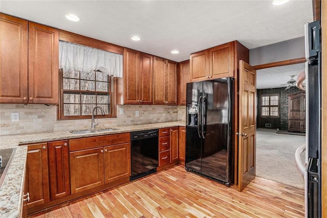 kitchen featuring light stone countertops, black appliances, light wood-style floors, and a sink