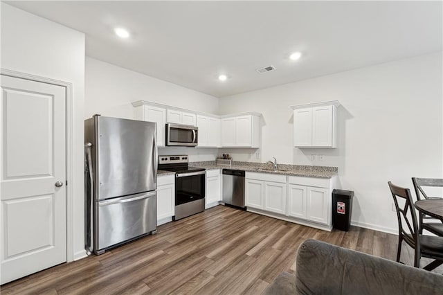 kitchen with light stone countertops, stainless steel appliances, dark wood-type flooring, sink, and white cabinetry