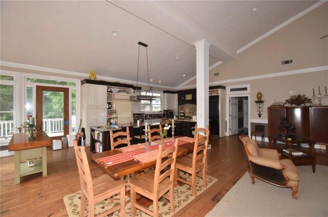 dining room featuring light hardwood / wood-style floors, lofted ceiling, ornamental molding, and ornate columns