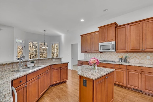 kitchen featuring hanging light fixtures, appliances with stainless steel finishes, a sink, and light stone countertops