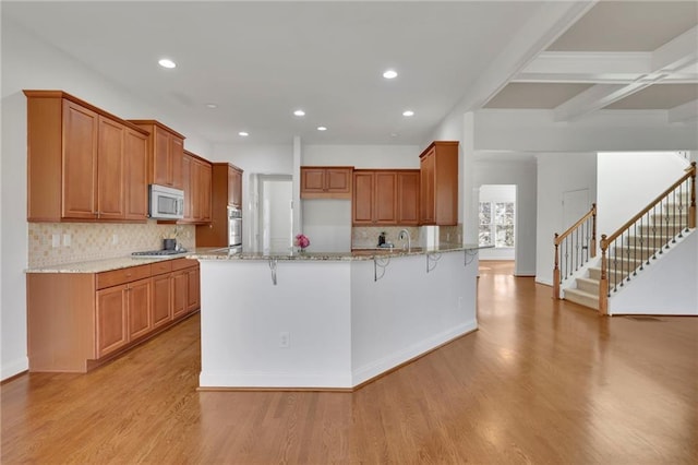 kitchen featuring brown cabinets, a breakfast bar area, appliances with stainless steel finishes, light stone countertops, and light wood-type flooring