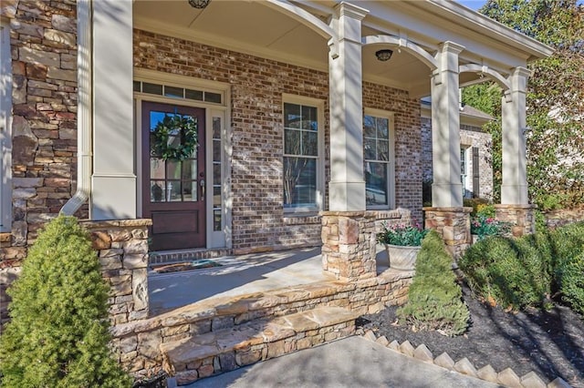 view of exterior entry with a porch and brick siding