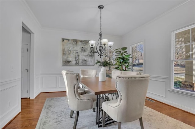 dining room featuring crown molding, a notable chandelier, a decorative wall, and wood finished floors