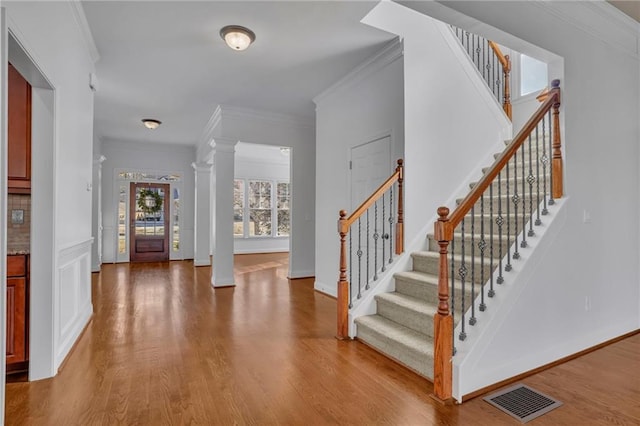 foyer with wood finished floors, visible vents, stairway, ornate columns, and crown molding