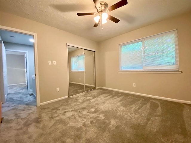 unfurnished bedroom with a textured ceiling, a closet, ceiling fan, and dark colored carpet