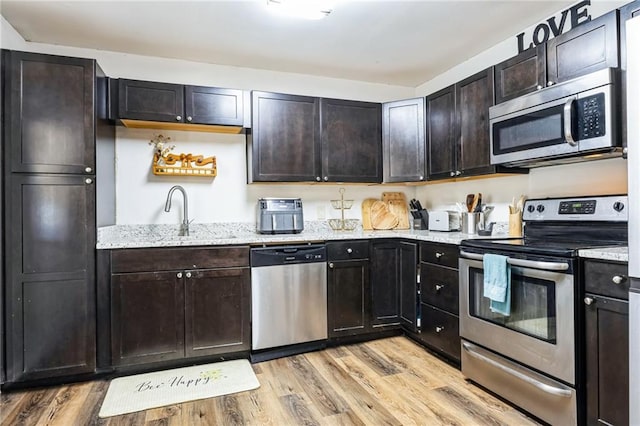 kitchen with appliances with stainless steel finishes, sink, dark brown cabinets, and light hardwood / wood-style flooring