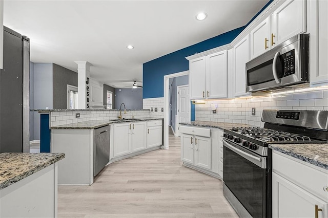 kitchen featuring stainless steel appliances, a sink, a peninsula, and light stone countertops