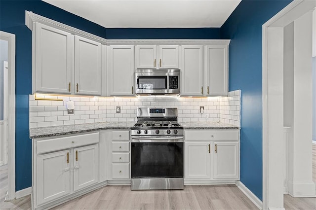 kitchen with light wood finished floors, appliances with stainless steel finishes, light stone counters, white cabinetry, and backsplash