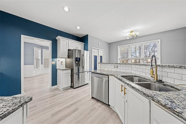 kitchen featuring light stone counters, appliances with stainless steel finishes, white cabinetry, a sink, and light wood-type flooring