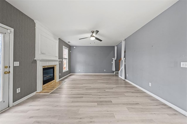 unfurnished living room with light wood-style floors, baseboards, a ceiling fan, and a glass covered fireplace