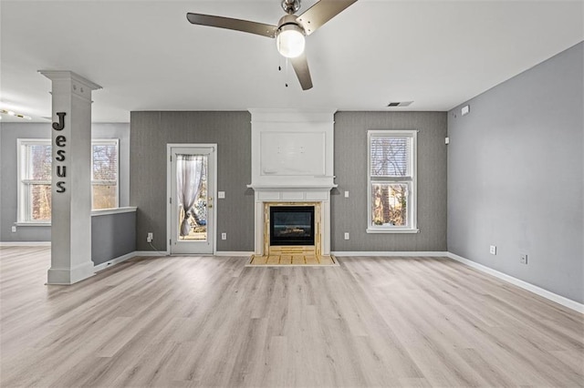 unfurnished living room with decorative columns, light wood-style floors, a ceiling fan, a large fireplace, and baseboards