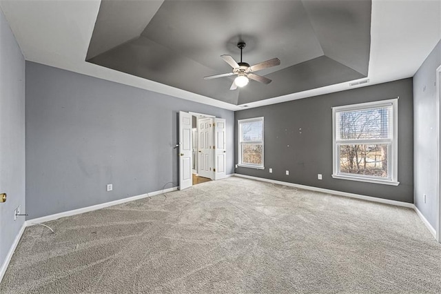 unfurnished bedroom with a tray ceiling, multiple windows, carpet flooring, and baseboards