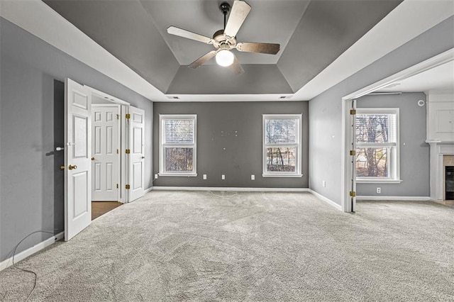 empty room with carpet floors, a tray ceiling, a premium fireplace, and baseboards