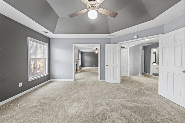 unfurnished bedroom featuring a ceiling fan, visible vents, baseboards, a tray ceiling, and carpet