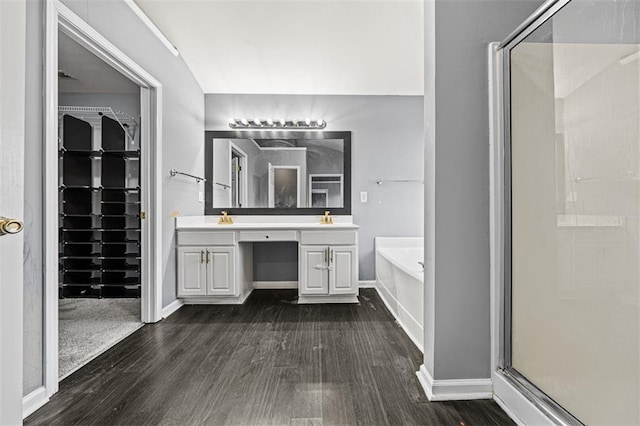 bathroom with a garden tub, double vanity, a spacious closet, a shower stall, and wood finished floors