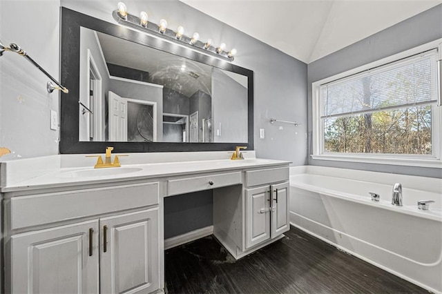 full bath with double vanity, a bath, wood finished floors, vaulted ceiling, and a sink