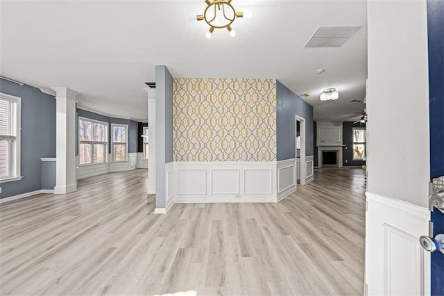 interior space featuring a wainscoted wall, a fireplace, visible vents, light wood finished floors, and decorative columns