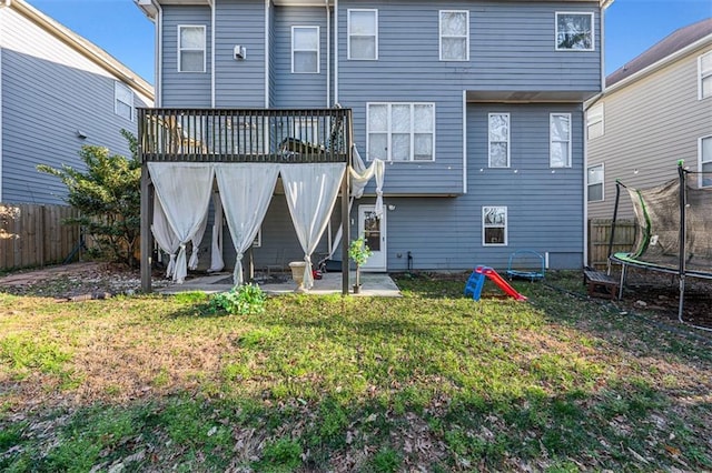 back of house featuring a trampoline, a lawn, a patio area, a deck, and a fenced backyard