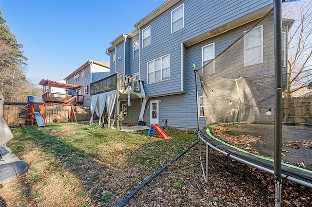 rear view of house featuring a trampoline, a playground, a patio, a lawn, and fence