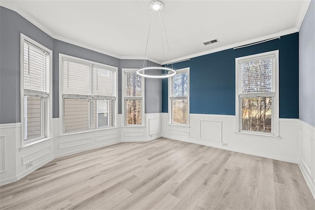 unfurnished dining area featuring wainscoting, visible vents, crown molding, and wood finished floors