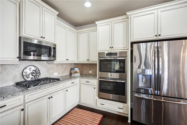 4155 Brookview Dr, Cumming, GA 30040 - kitchen featuring appliances with stainless steel finishes, light stone counters, white cabinetry, dark wood-type flooring, and decorative backsplash