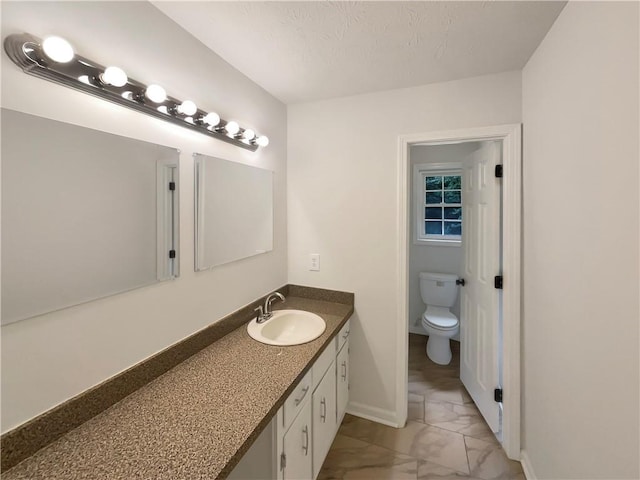 bathroom with vanity, toilet, baseboards, and marble finish floor