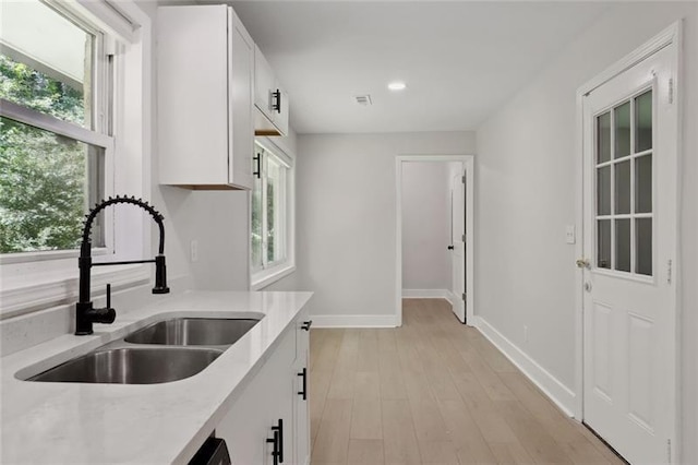 kitchen with a sink, white cabinets, a wealth of natural light, and light countertops