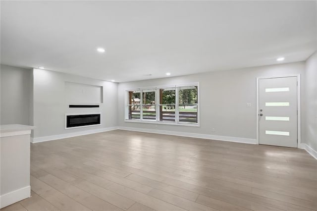 unfurnished living room with a glass covered fireplace, baseboards, recessed lighting, and light wood-type flooring