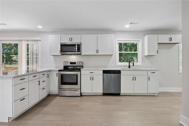 kitchen featuring a sink, light countertops, white cabinets, a peninsula, and stainless steel appliances
