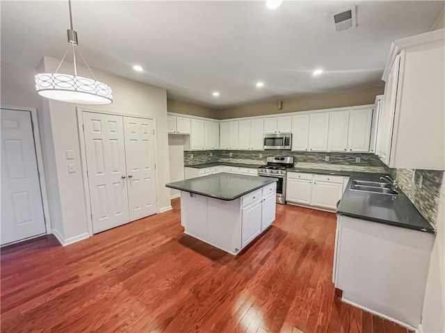 kitchen featuring decorative light fixtures, stainless steel appliances, dark countertops, white cabinetry, and a kitchen island