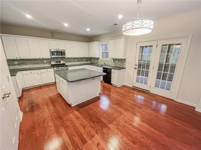 kitchen featuring stainless steel appliances, a kitchen island, white cabinets, dark countertops, and pendant lighting