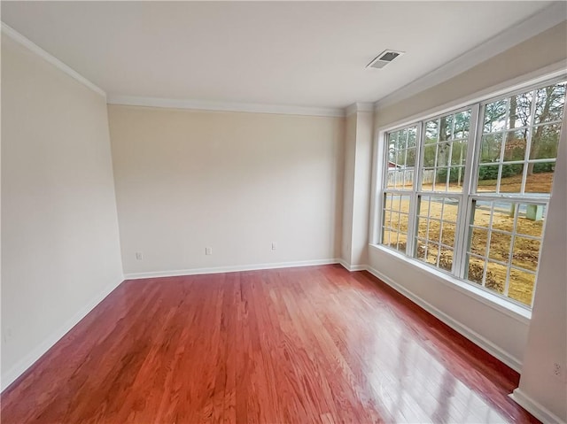 spare room with ornamental molding, wood finished floors, visible vents, and baseboards