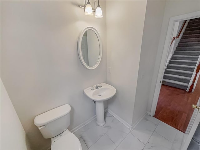 half bath with toilet, marble finish floor, and baseboards