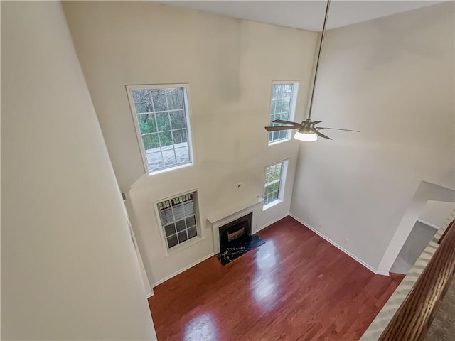 unfurnished living room featuring dark wood-style flooring, a fireplace, a towering ceiling, a ceiling fan, and baseboards