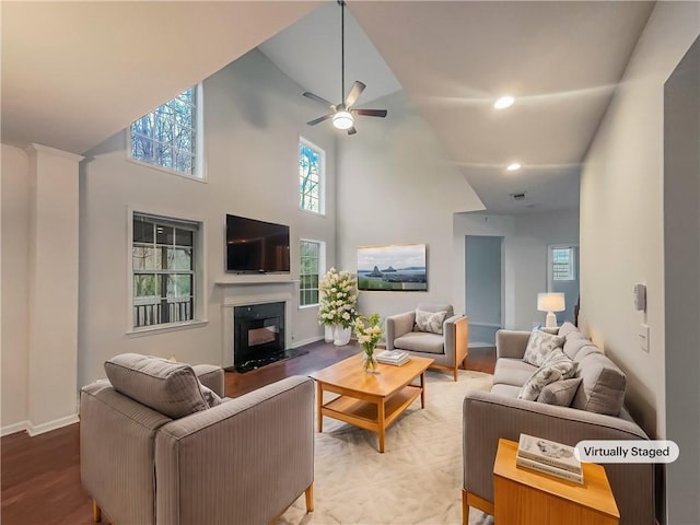 living area featuring ceiling fan, wood finished floors, a towering ceiling, a high end fireplace, and baseboards