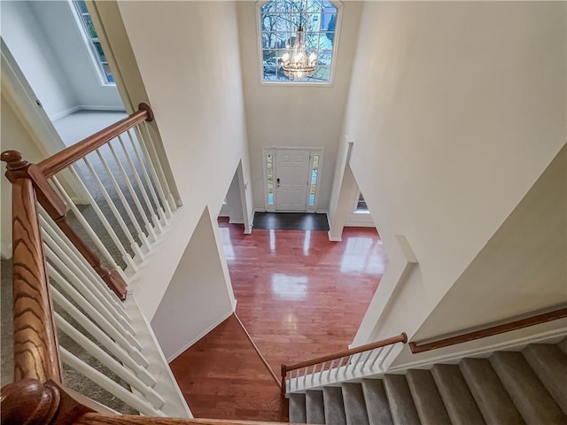 stairs with a healthy amount of sunlight, a high ceiling, a chandelier, and wood finished floors