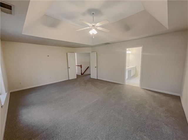 unfurnished bedroom with carpet floors, a tray ceiling, ensuite bath, and baseboards