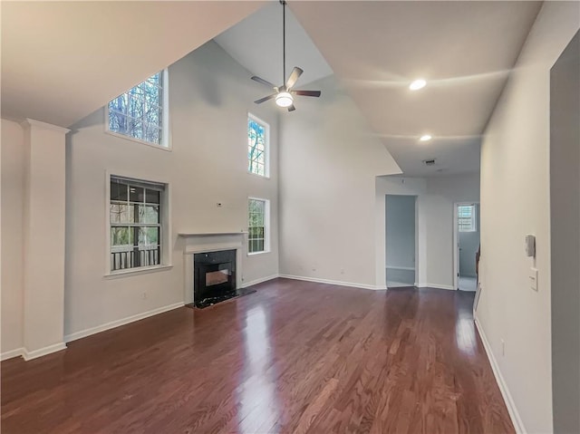 unfurnished living room with ceiling fan, dark wood-type flooring, a fireplace, a towering ceiling, and baseboards