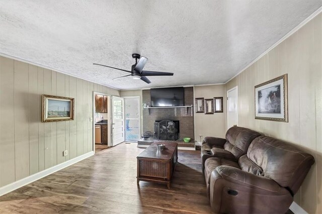 living room with a brick fireplace, a textured ceiling, ceiling fan, crown molding, and hardwood / wood-style floors