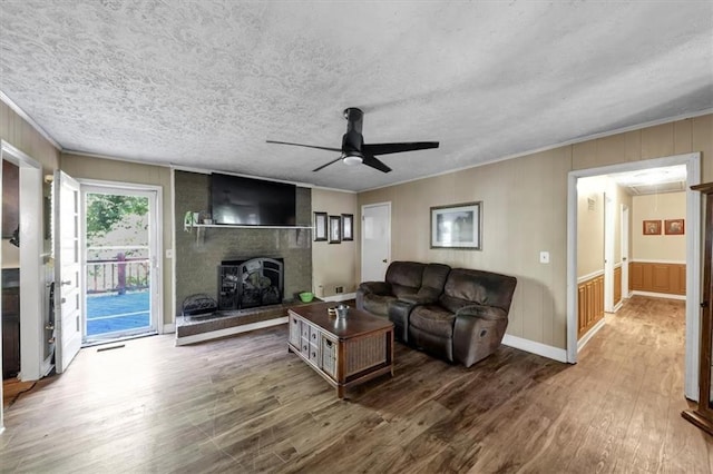 living room with ceiling fan, wood-type flooring, a textured ceiling, a fireplace, and ornamental molding