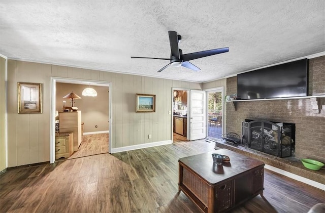 living room with a brick fireplace, a textured ceiling, ceiling fan, crown molding, and hardwood / wood-style flooring