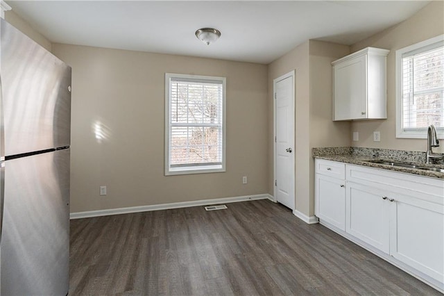 kitchen with stone counters, visible vents, freestanding refrigerator, white cabinets, and a sink