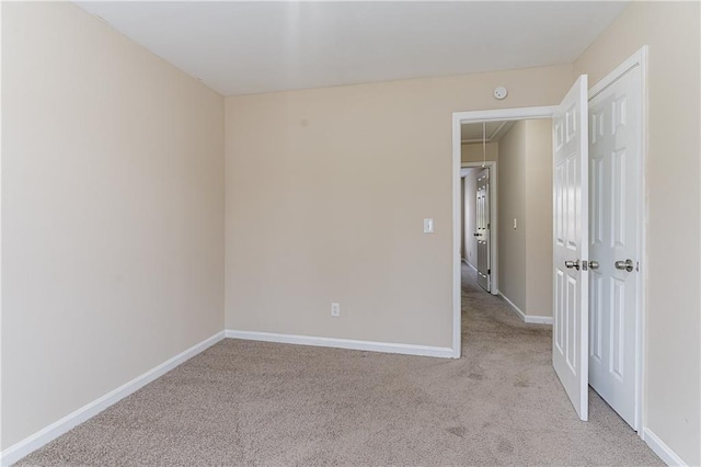 empty room with attic access, baseboards, and light colored carpet