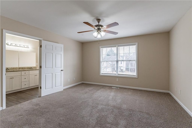 unfurnished bedroom featuring baseboards, ceiling fan, ensuite bathroom, and light colored carpet