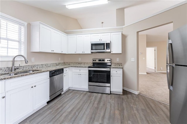 kitchen featuring appliances with stainless steel finishes, white cabinets, a sink, light stone countertops, and light wood-type flooring