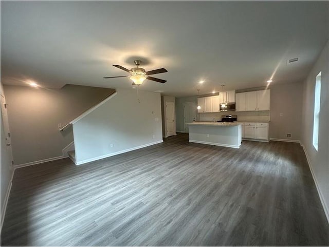 unfurnished living room with baseboards, a ceiling fan, dark wood-style flooring, stairs, and a sink