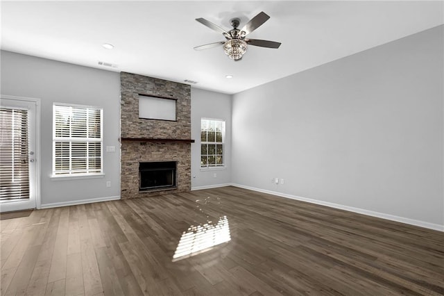 unfurnished living room with ceiling fan, a stone fireplace, and dark hardwood / wood-style flooring